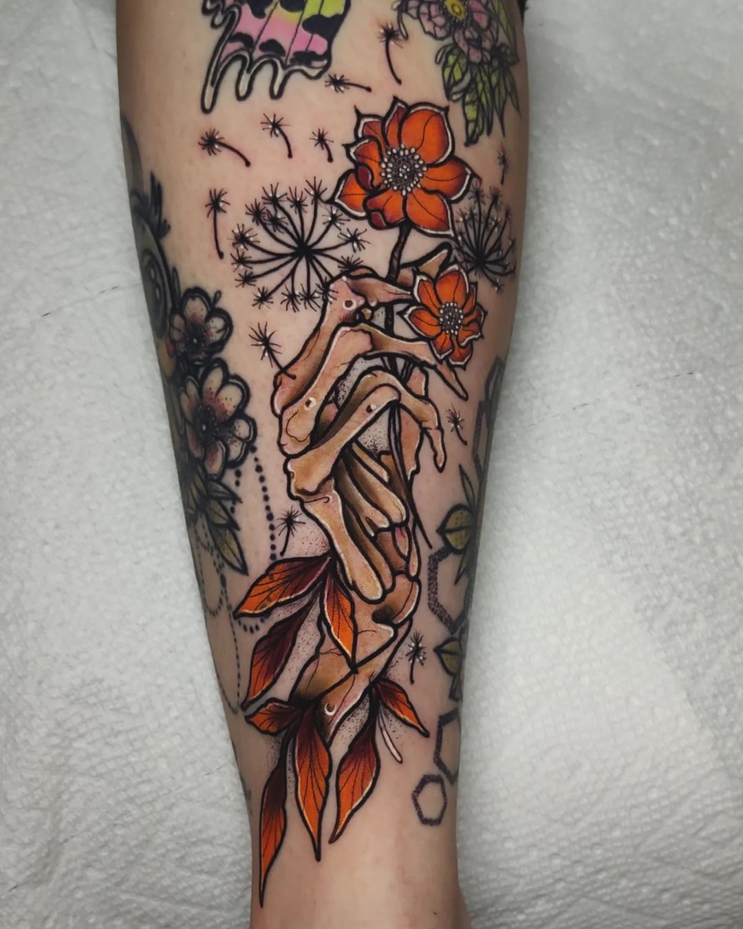 Skeletal hand holding wildflowers, forearm tattoo